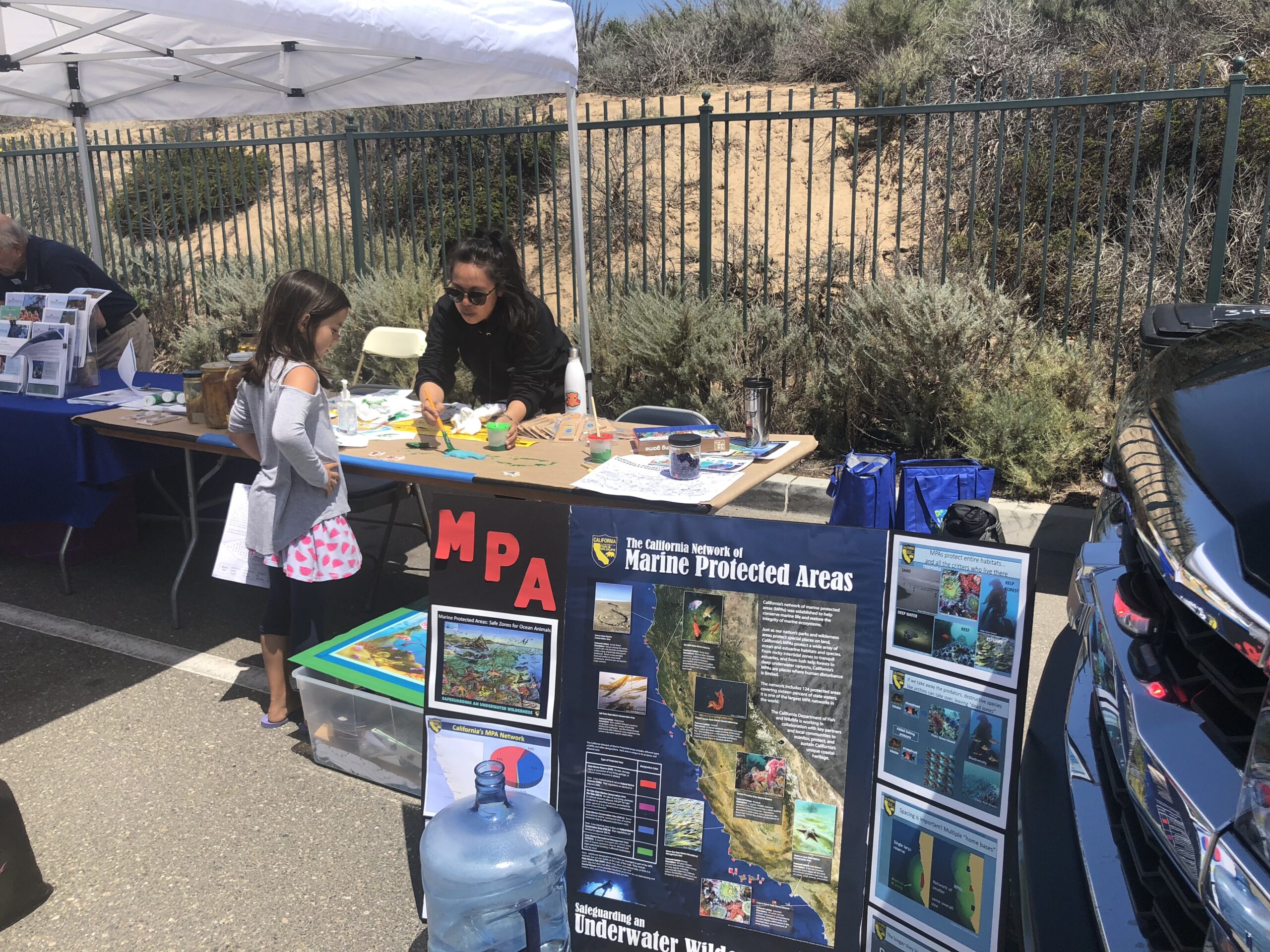 Image shows a poster display of Marine Protected Areas in front of a tabling set up, showing a little girl learning something at the table from an adult behind the table.
